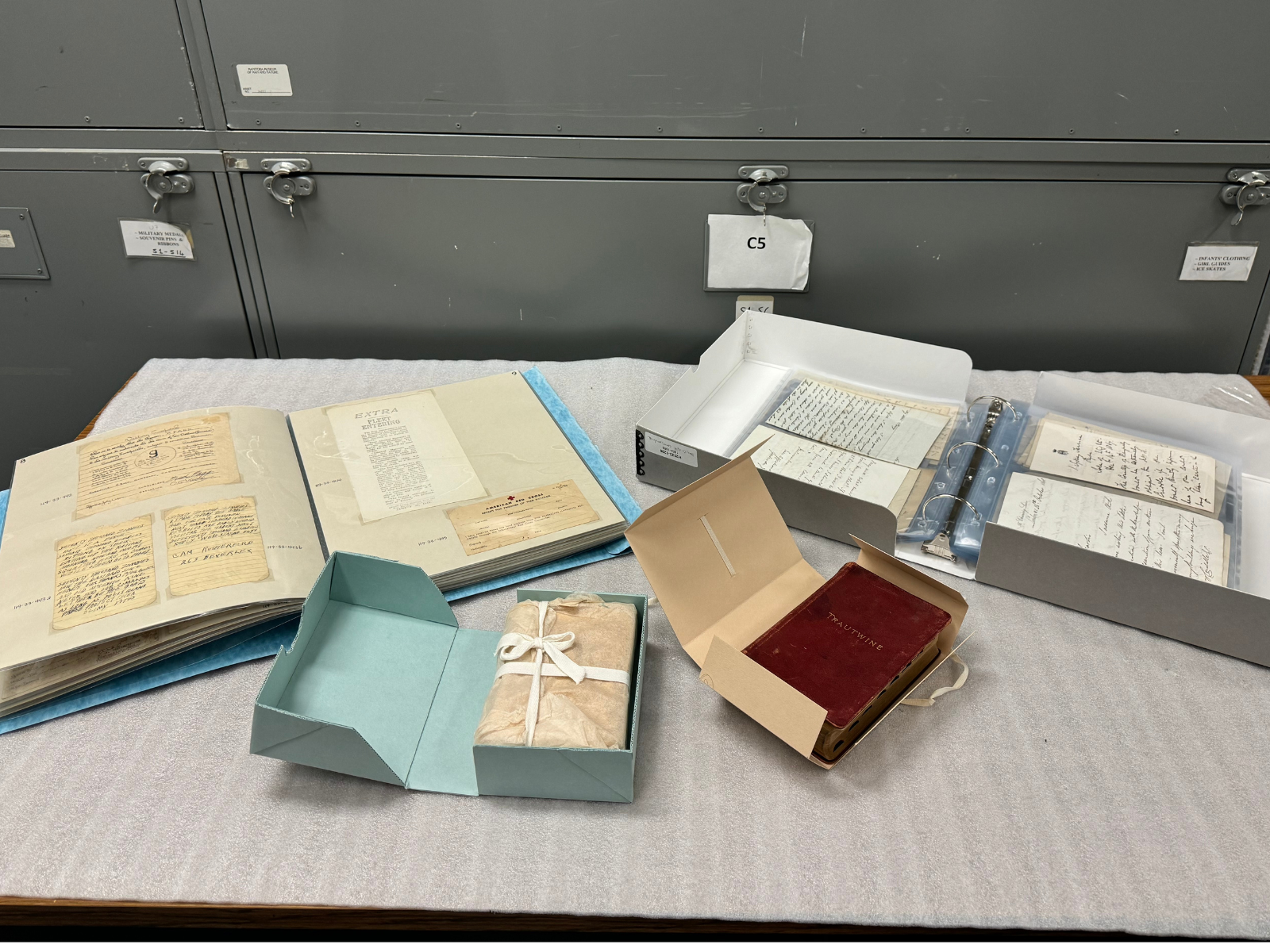 Four objects including several books and a binder that are themselves artifacts or contain and store artifacts. Each is place in a close fitting, folding box to support preservation.