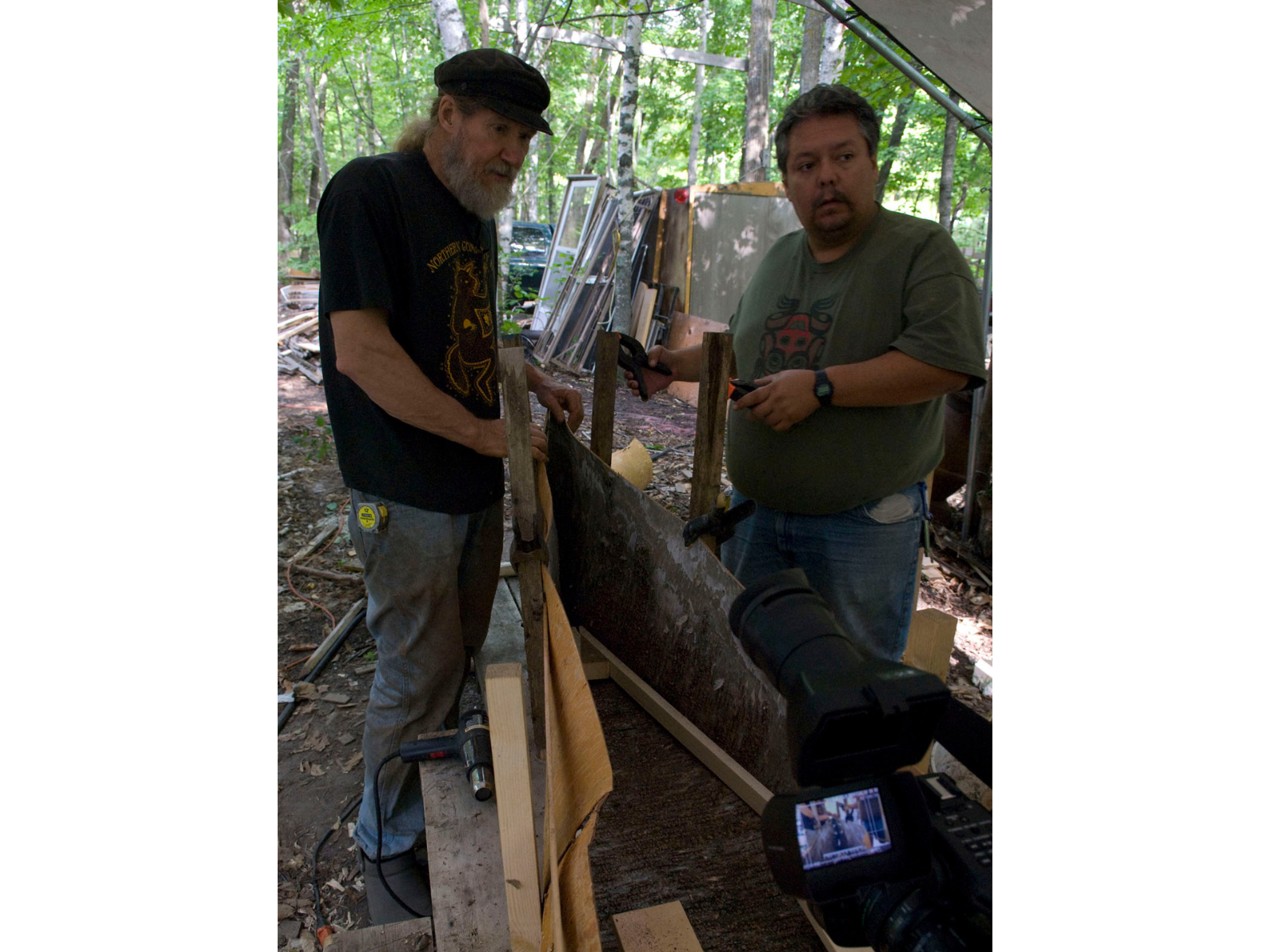 Two individuals inspecting a braced canoe frame from the one end.