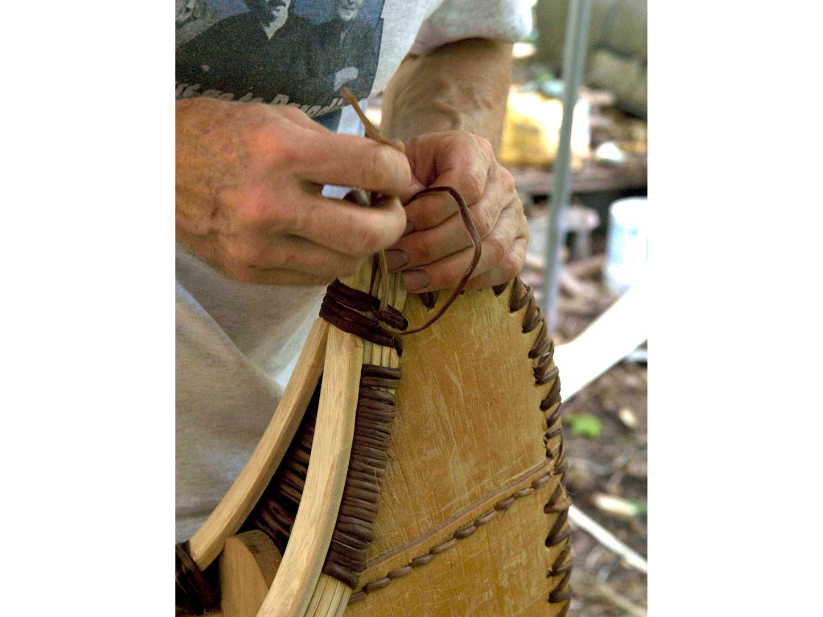 Hands reach into frame stitching with thick material closing the edge end of a canoe.