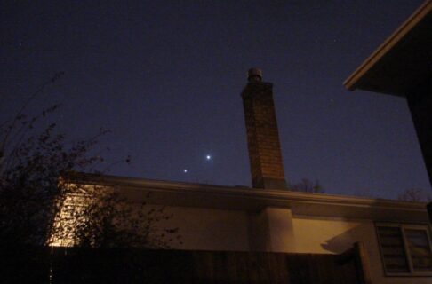 Two bright lights in the night sky over a rooftop.