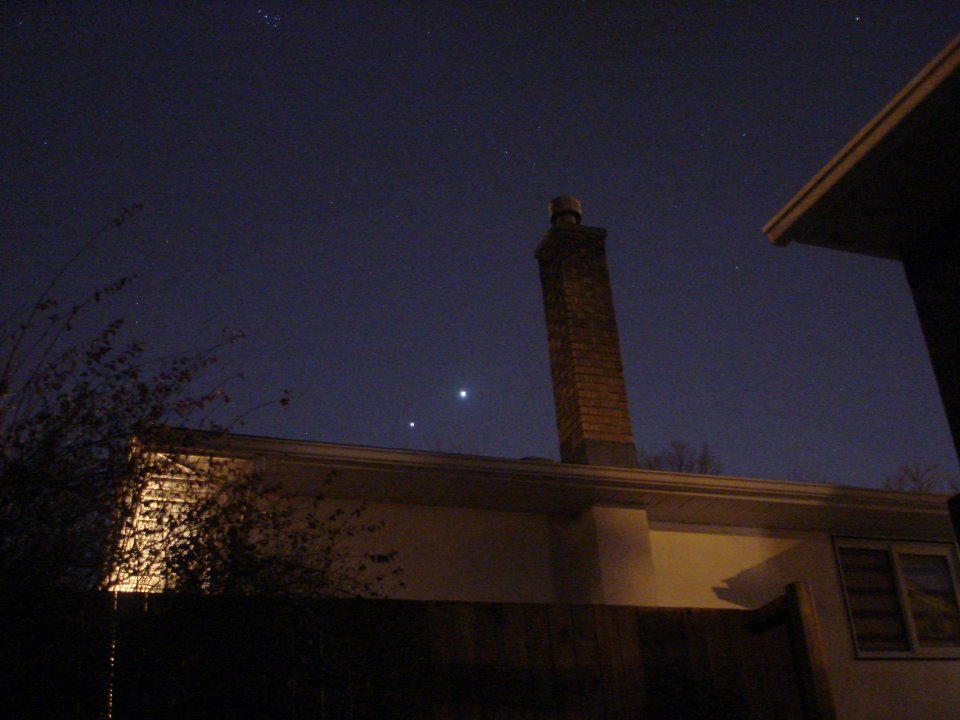 Two bright lights in the night sky over a rooftop.