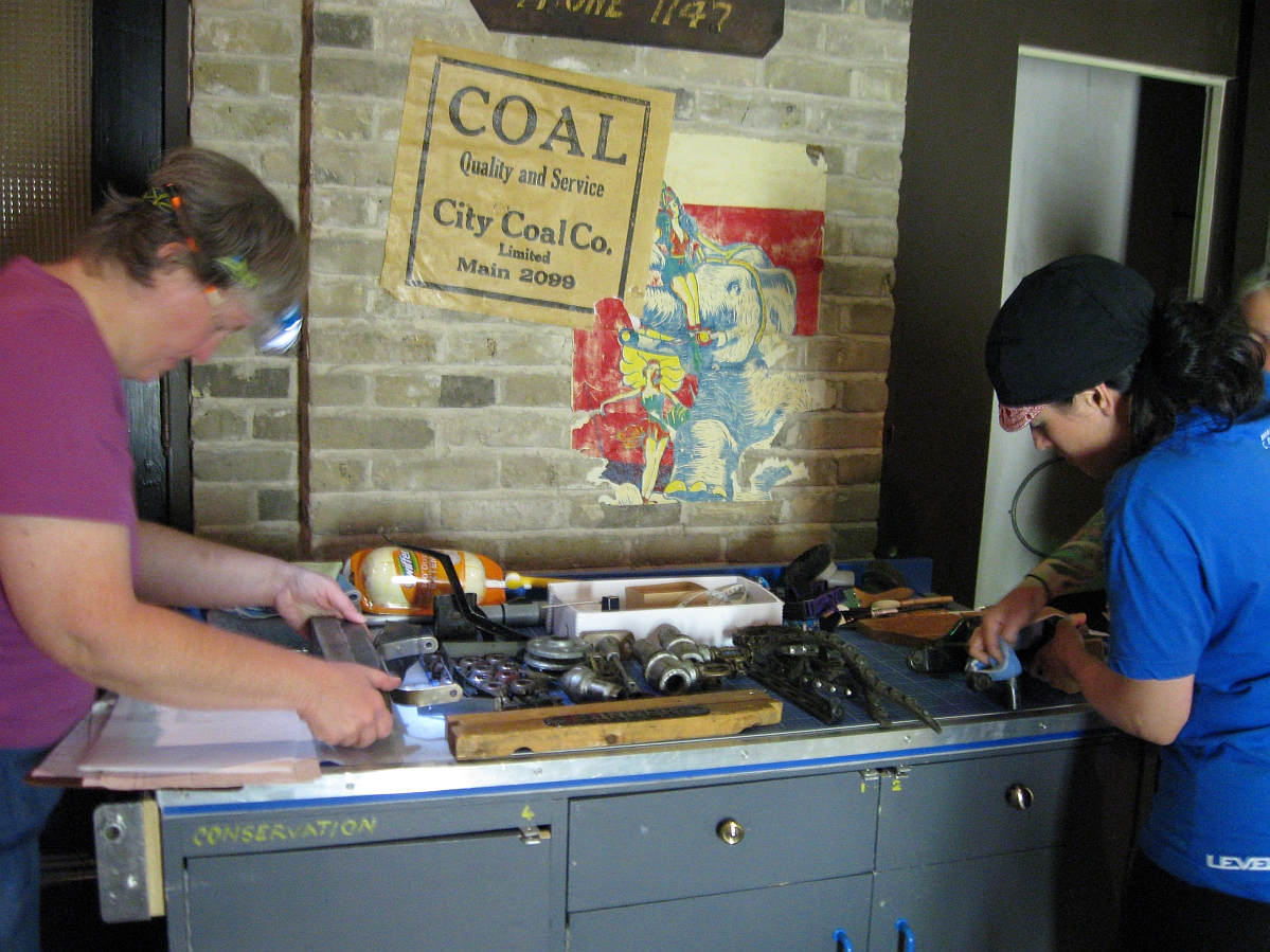 Three staff members standing around a work bench on wheels, checking on artifacts.