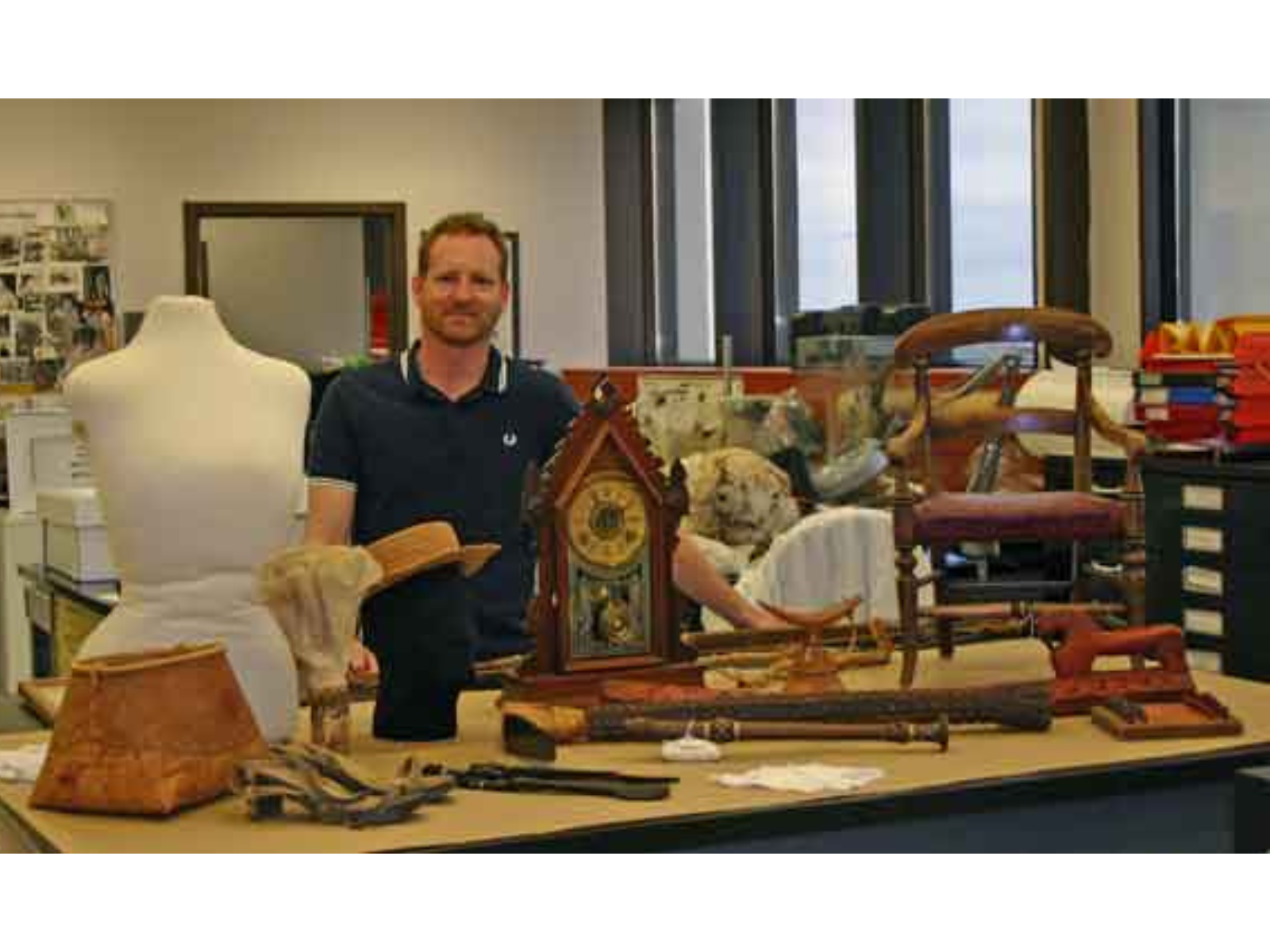 An individual standing behind a table in a lab that is spread with artifacts.