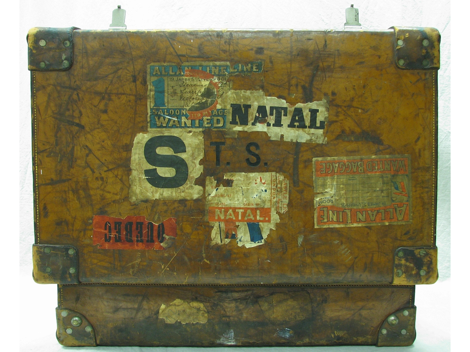 An aged open trunk or large suitcase with the open lid facing the camera. Various worn stickers and labels are peeling around the lid.