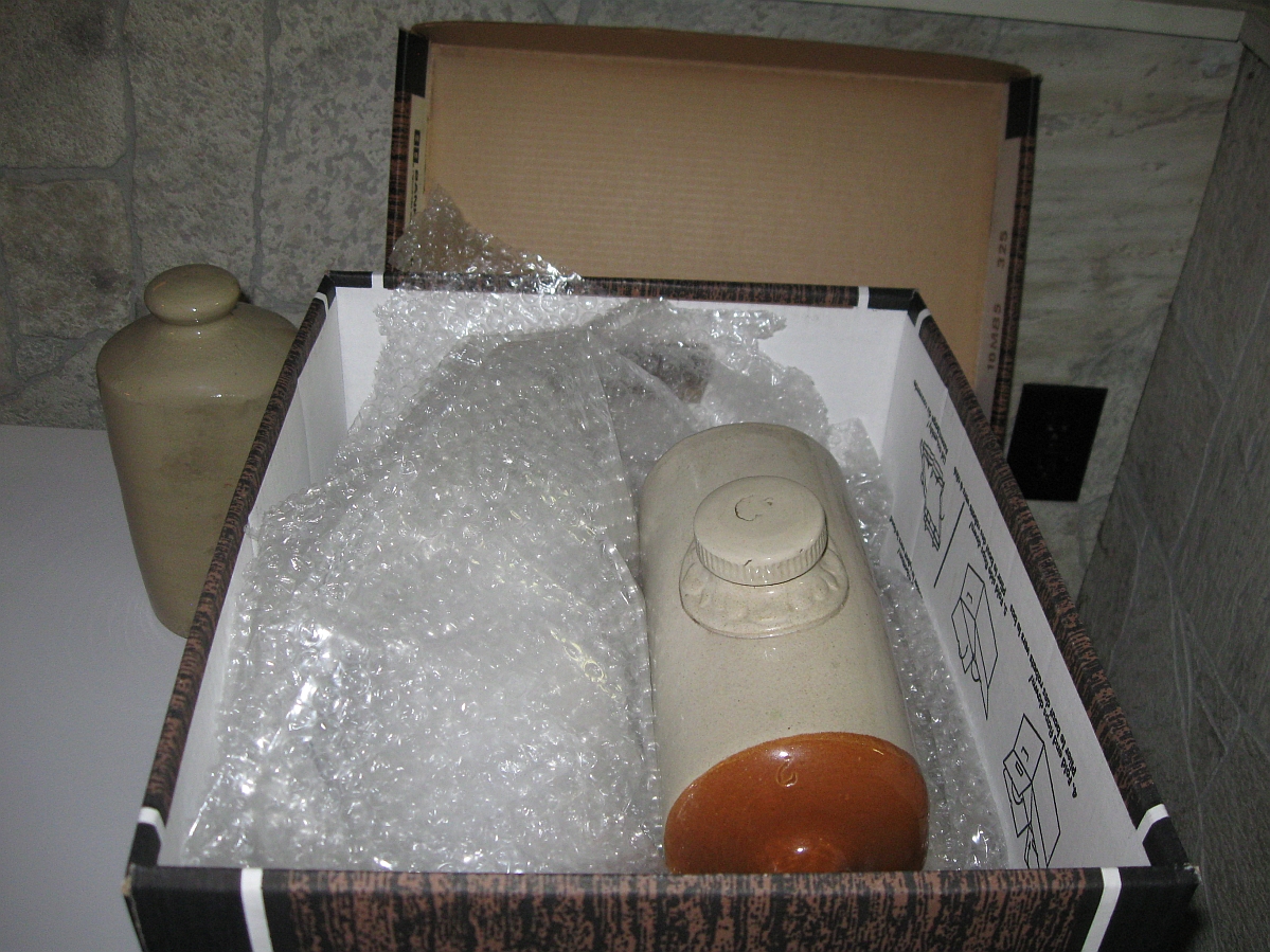 Two ceramic footwarmers wrapped in bubble wraps in a box.