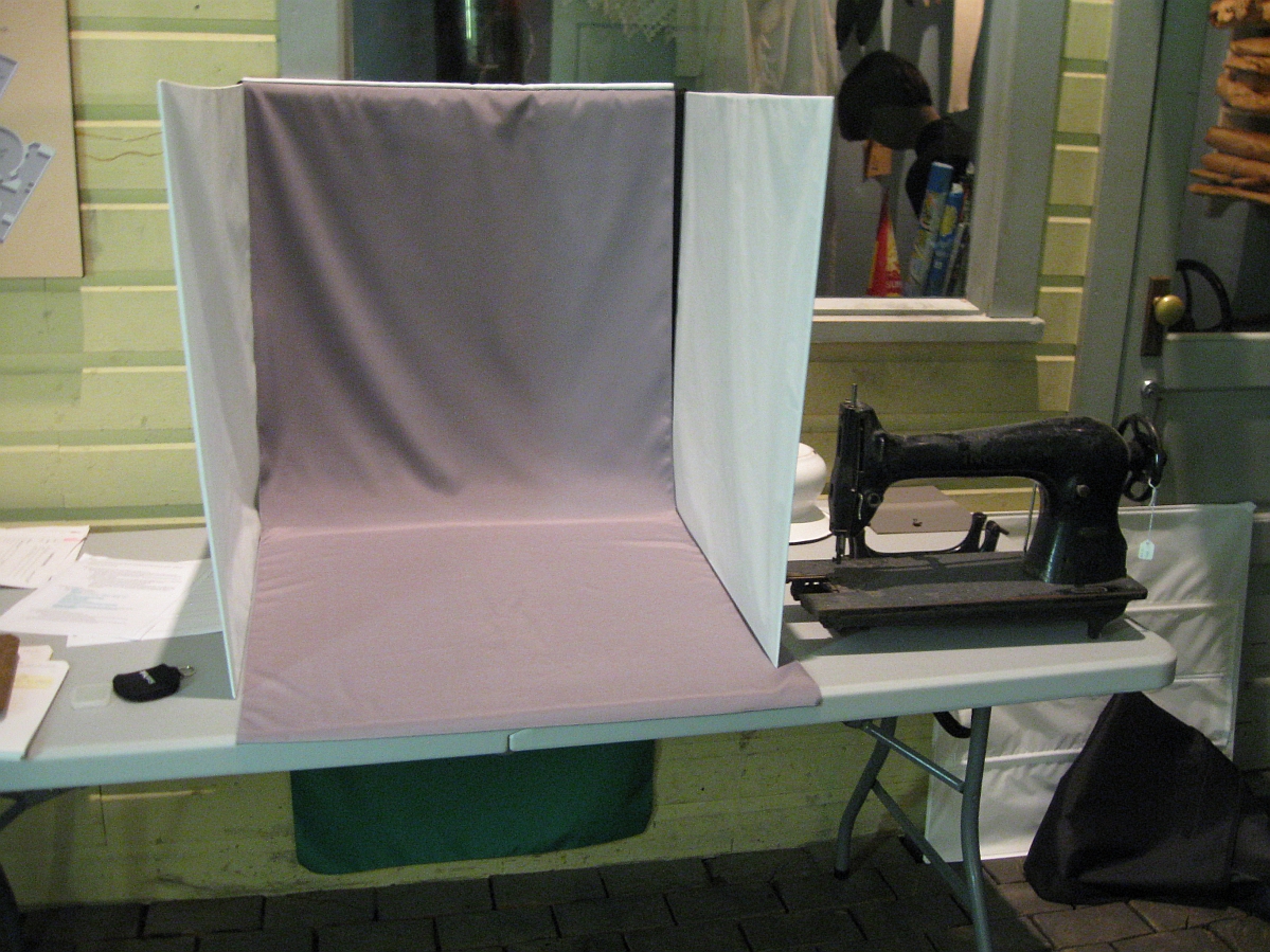 A shadow box set up on a table with a strip of light purple-grey cloth draped along the base and backside. Beside it on the table sits an old fashioned sewing machine.