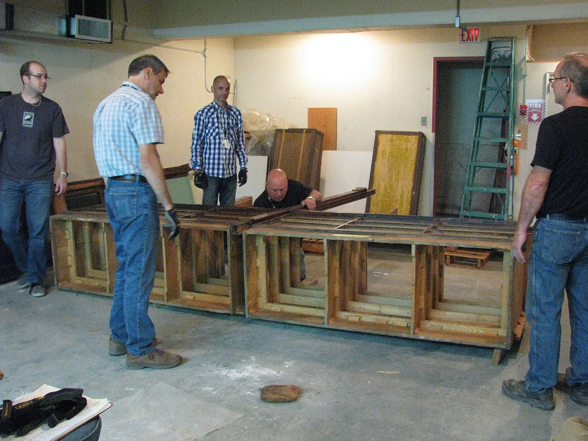 Five individuals standing around the frame of a large display case laying on its side on the ground.