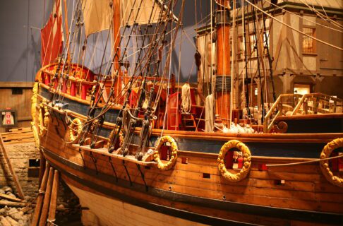 View of the side exterior of a wooden sailing vessel in a museum gallery.