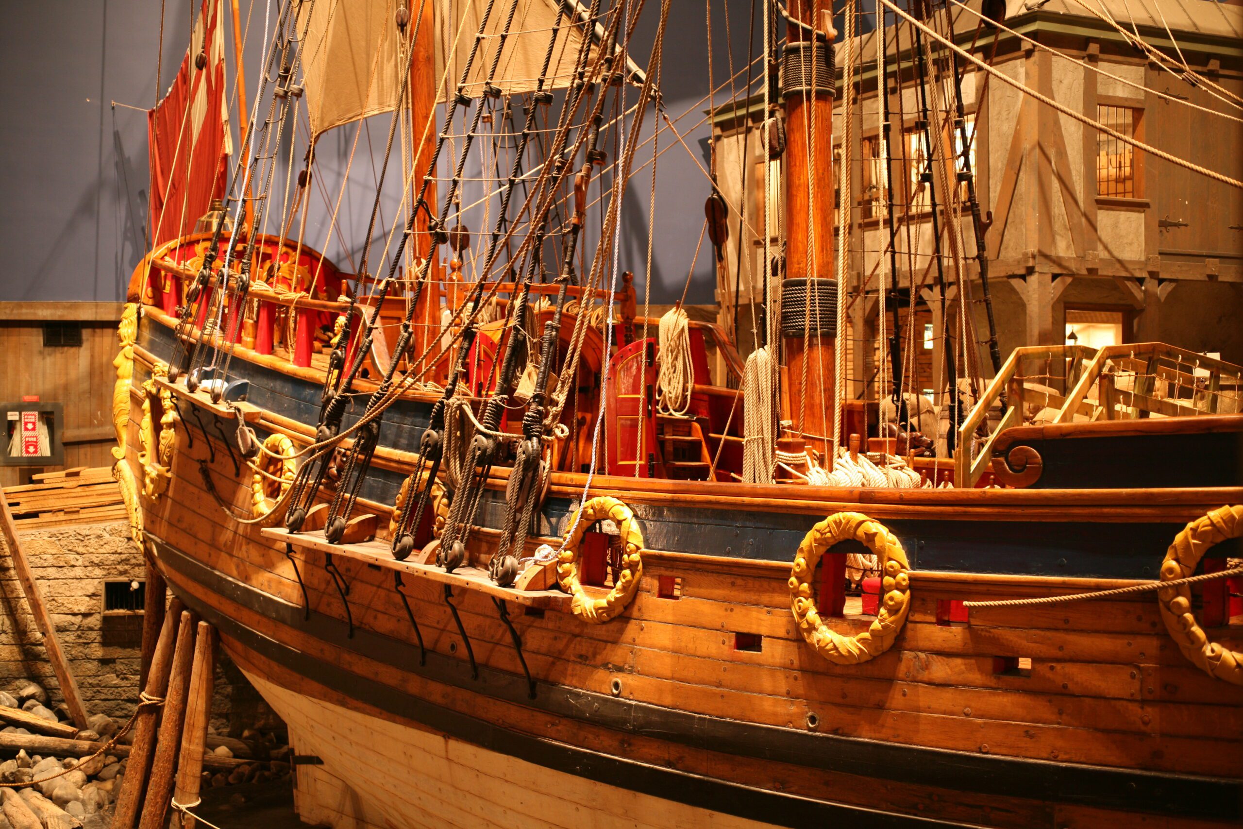 View of the side exterior of a wooden sailing vessel in a museum gallery.