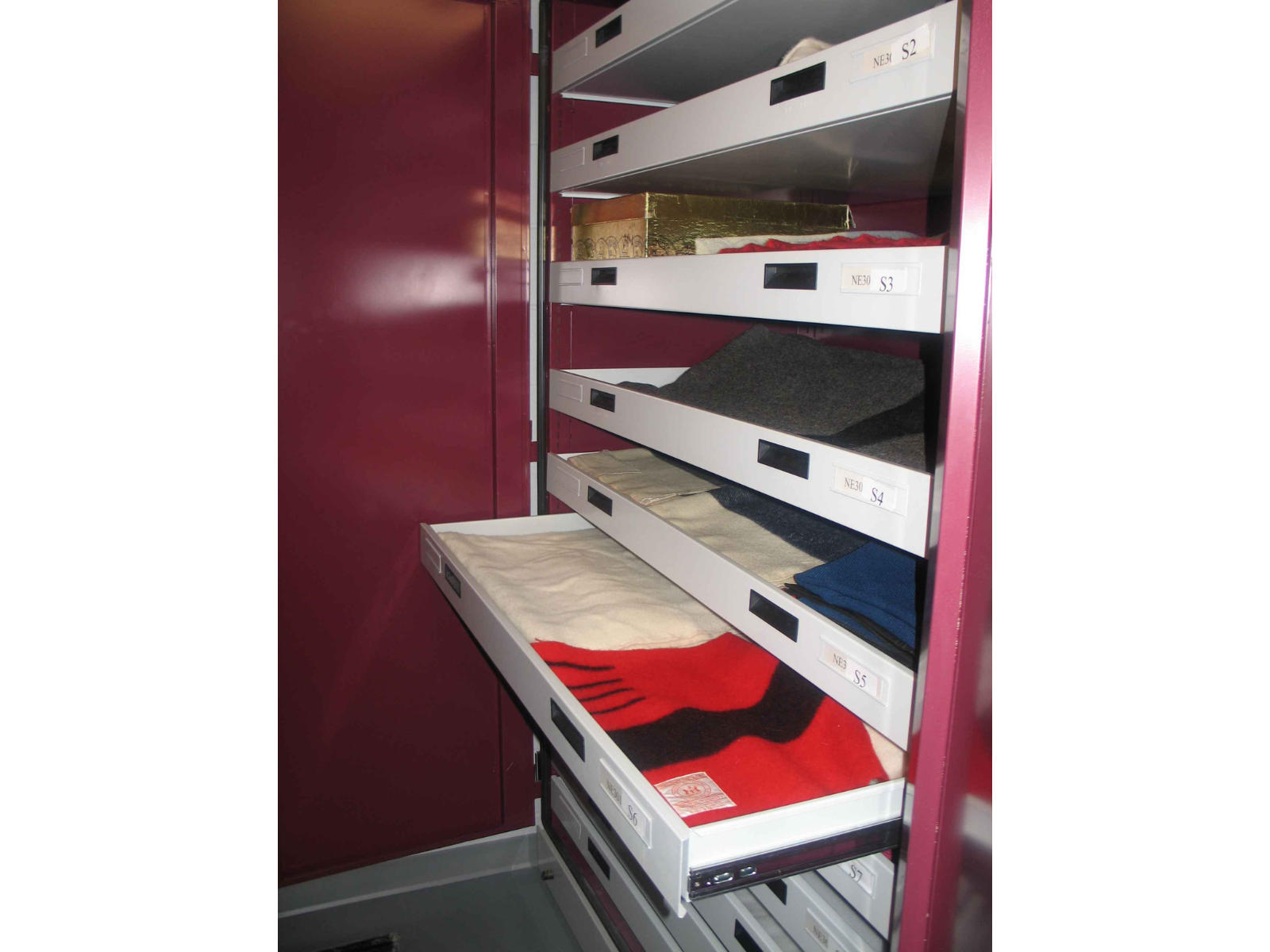 An open cabinet with spaced out drawers. One is opened revealing woolen blankets.