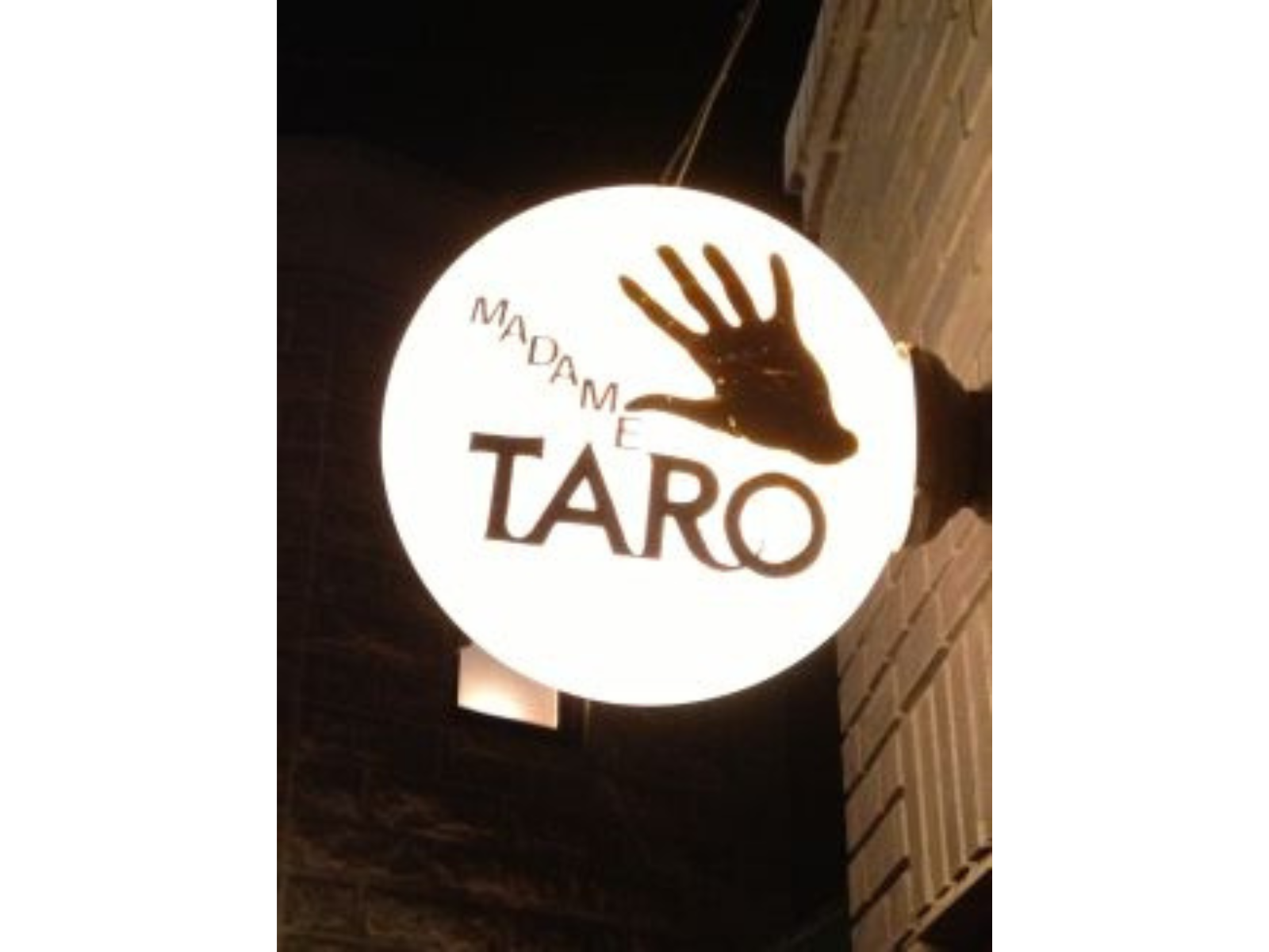 Close up on an illuminated sign with a handprint and text reading "Madame Taro".