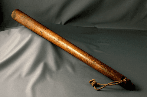 A wooden club with a strap at the base, against a grey background.