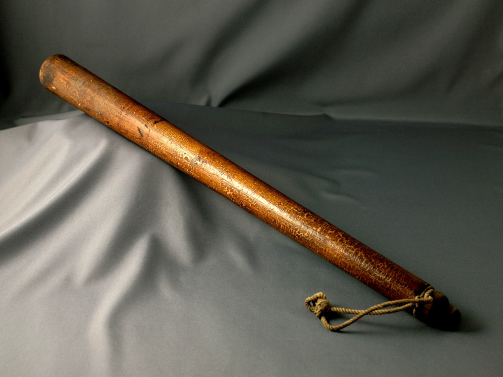 A wooden club with a strap at the base, against a grey background.