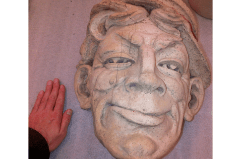 A large terra cotta face, with a hand beside it in the lower left corner for scale.