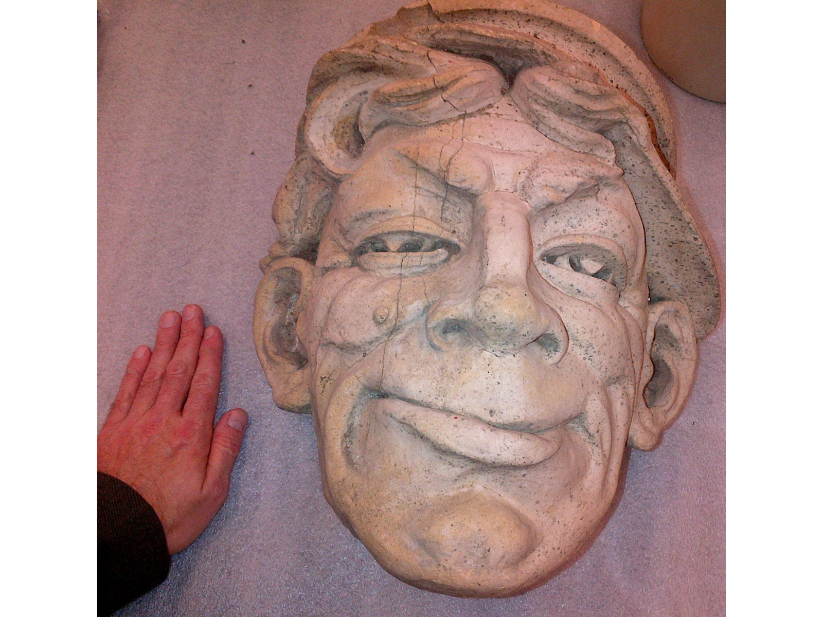 A large terra cotta face, with a hand beside it in the lower left corner for scale.