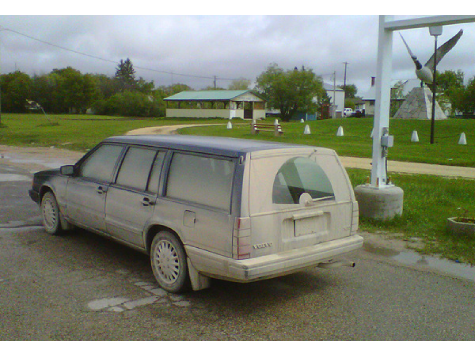 A very dirty, dusty car parked next to a field with a large Canada goose statue.