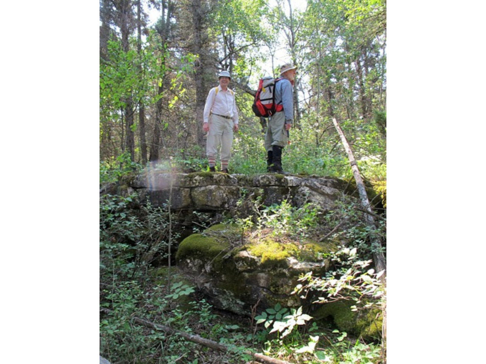 Two individuals on the top of a rocky outcropping in a treed area. Both are wearing their pants tucked into their long socks.