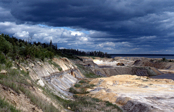 A landscape looking out over the cliffside of a stretch of land leading down to a shoreline. The sky is dramatically lit with thick clouds in shades of light and dark blue.