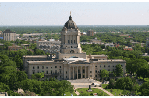 An aerial view of the Manitoba Legislative Building - a large building with a central tower ending in a dome with a gold statue at the top.