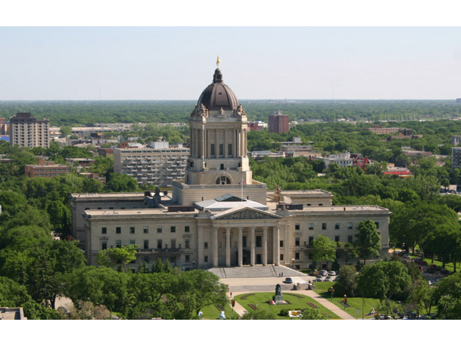 An aerial view of the Manitoba Legislative Building - a large building with a central tower ending in a dome with a gold statue at the top.