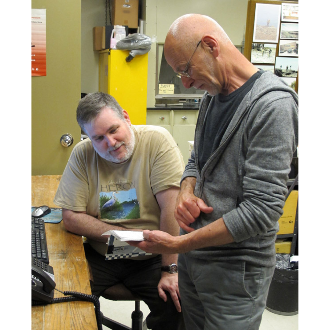 Two individuals in discussion in an office over a notebook.