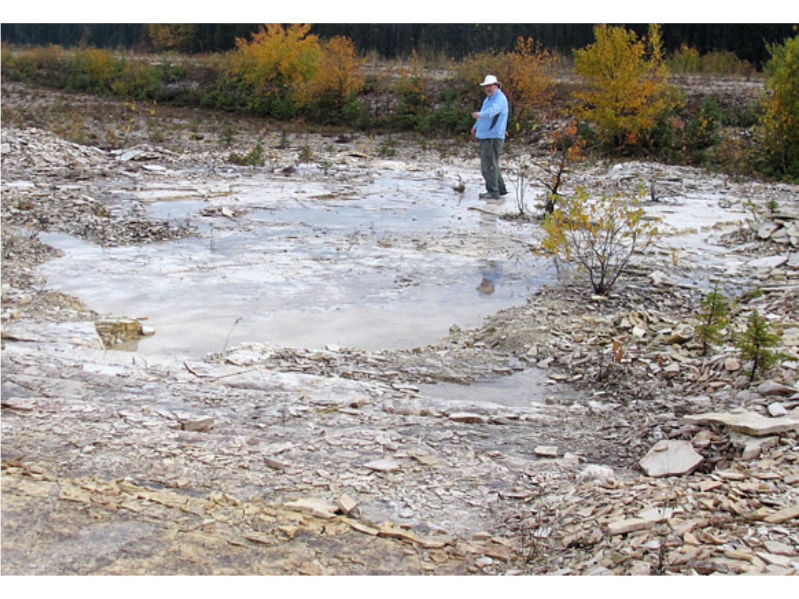 An individual standing across a large puddle on a rocky ground.