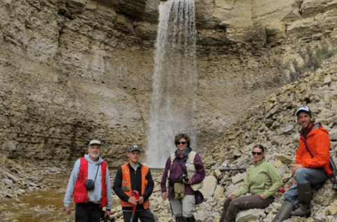 Five people posing together in front of a waterfall on the rocky shore of a creek.