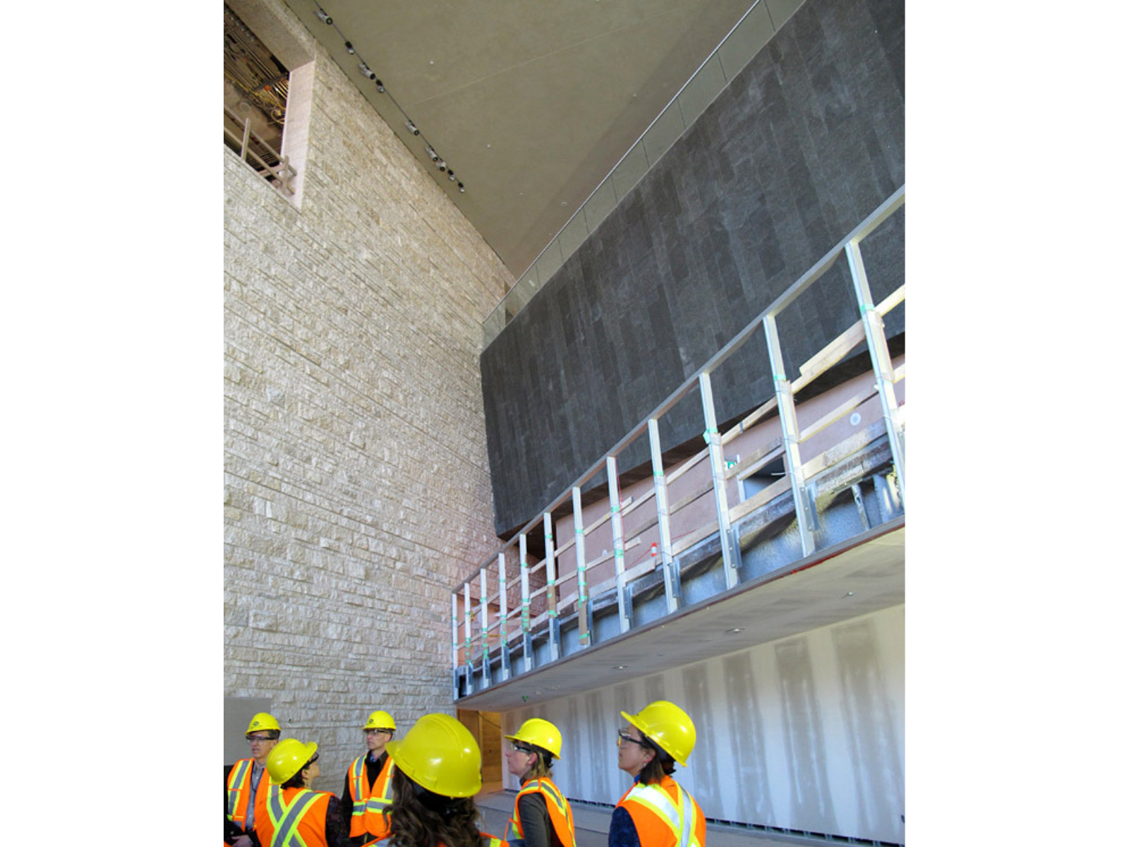 A group of individuals wearing high-vis vests and hard hats near the exterior wall of a large stone building under construction.