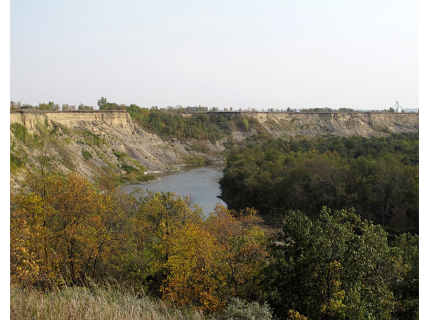 View towards a gorge with a river flowing through the centre. Green and yellow folliaged trees grow either side.