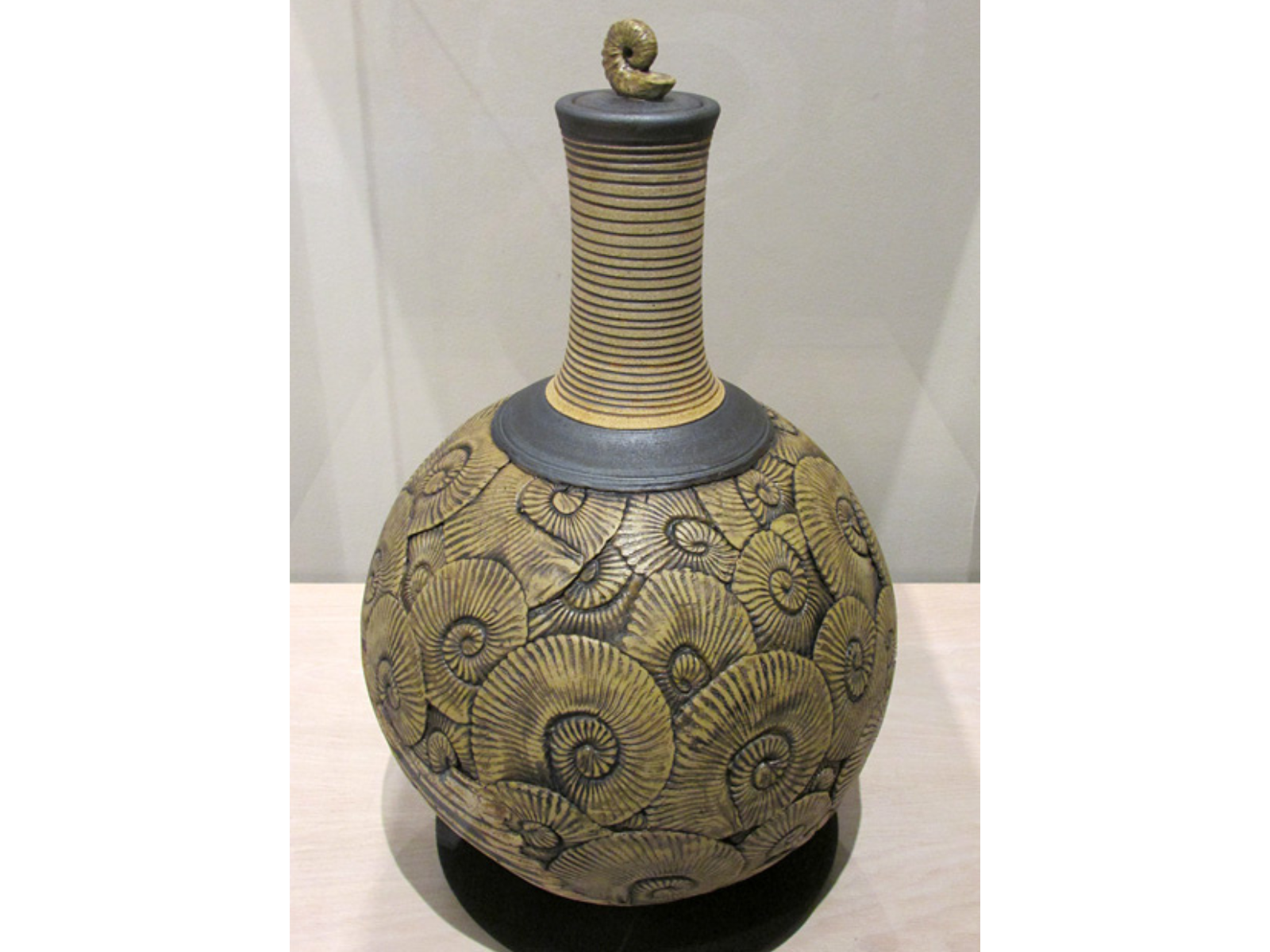 An elaborately engraved vase covered in black ammonoid designs with a small ammonoid at the top of the urn lid.