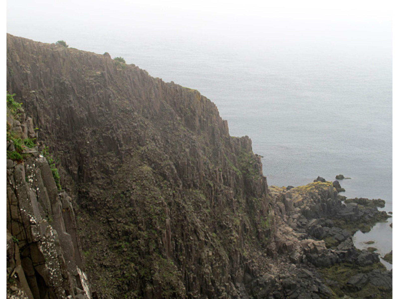 View of a large rocky hillside next to a body of water with incoming mist.