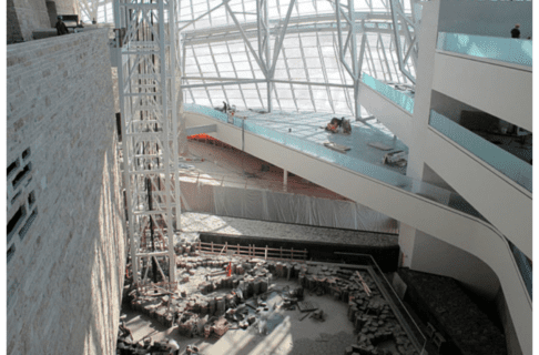 View from several stories up, looking down towards a space with rock-lined water elements. The area is well lit by large wall to wall windows.