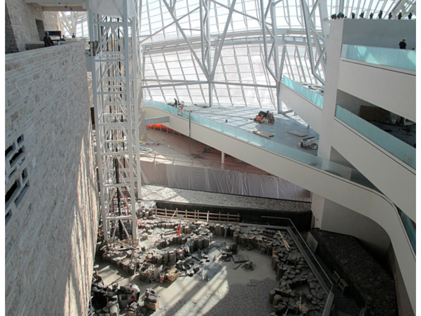 View from several stories up, looking down towards a space with rock-lined water elements. The area is well lit by large wall to wall windows.