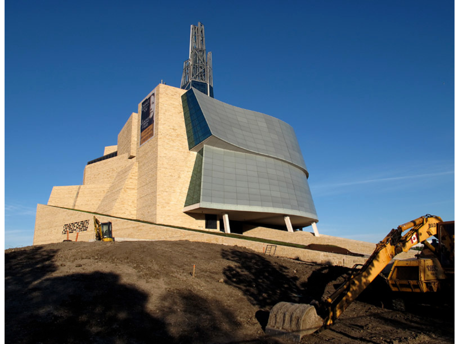 A large irregularly shaped building that is almost shaped like an upward growing spiral building to a central tower. The left side is a light tan stone and the right side is predominantly windows.