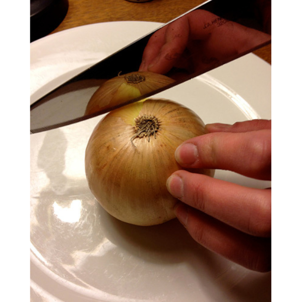 A whole onion on a plate with a hand holding a knife blade to the side of the onion in preparation of slicing.