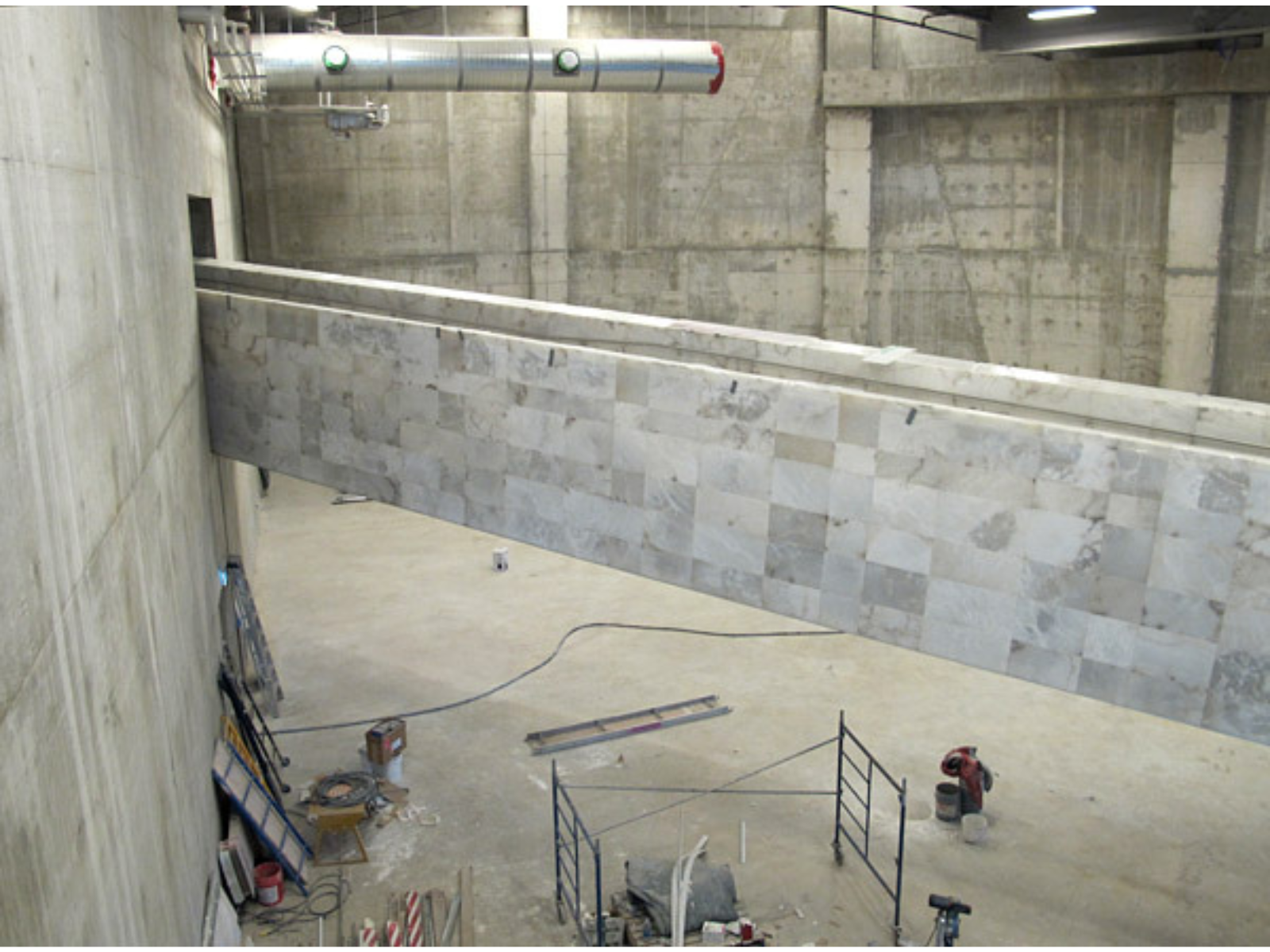 A stone room with a ramp crossing the centre. The room is under construction with carious tools and equipment on the main floor.