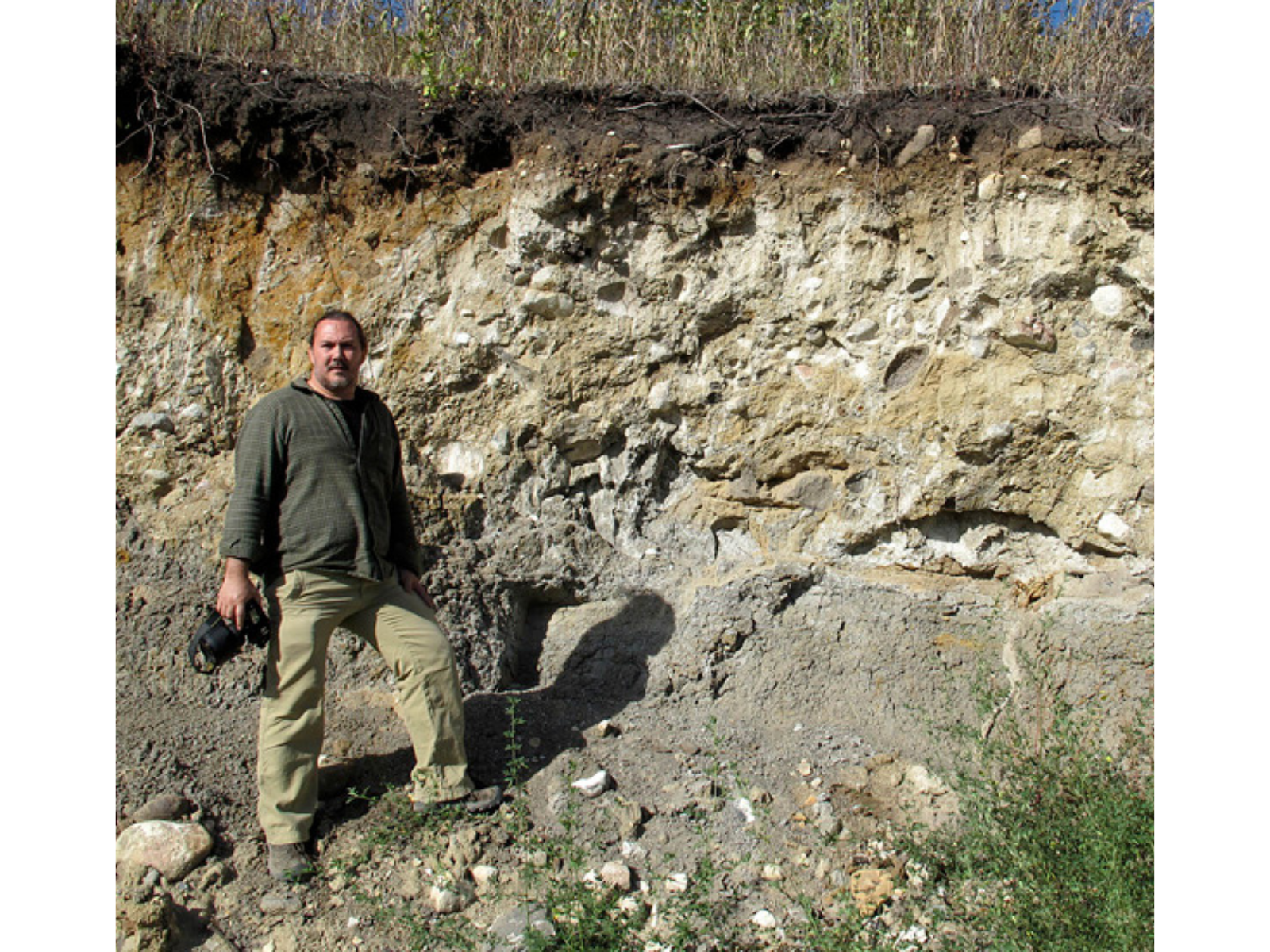 An individual stands beside a cut of ground beside a bank higher than themselves.