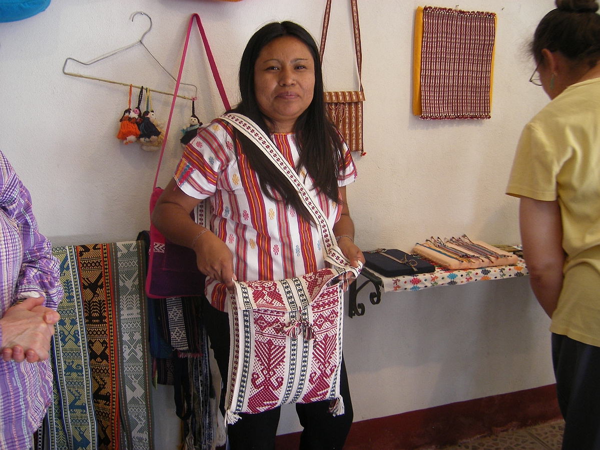 A smiling woman posing with a shoulder bag with an intricate woven pattern in red and white.
