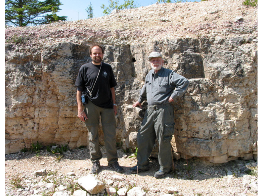 Two individuals standing in front of a large rocky wall.