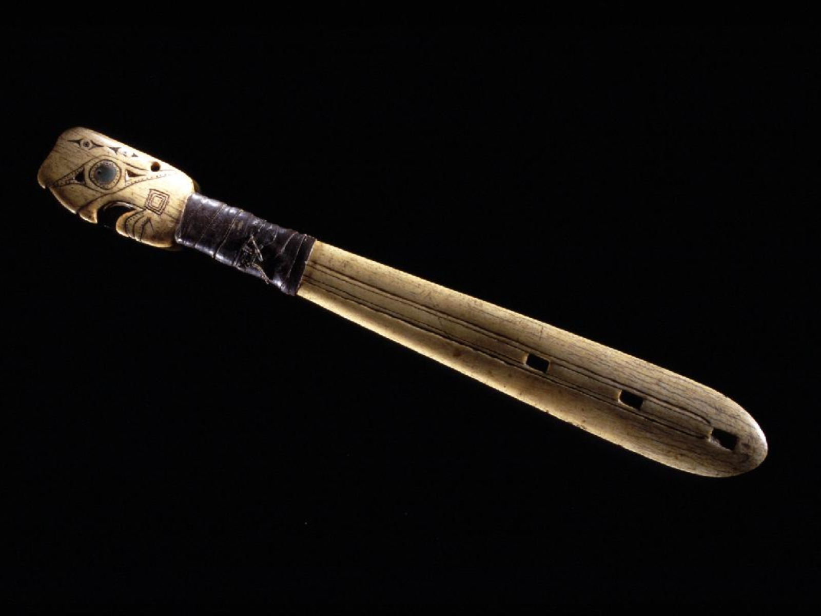 A whalebone club with a wrapped handle above a carved face at the base of the club.