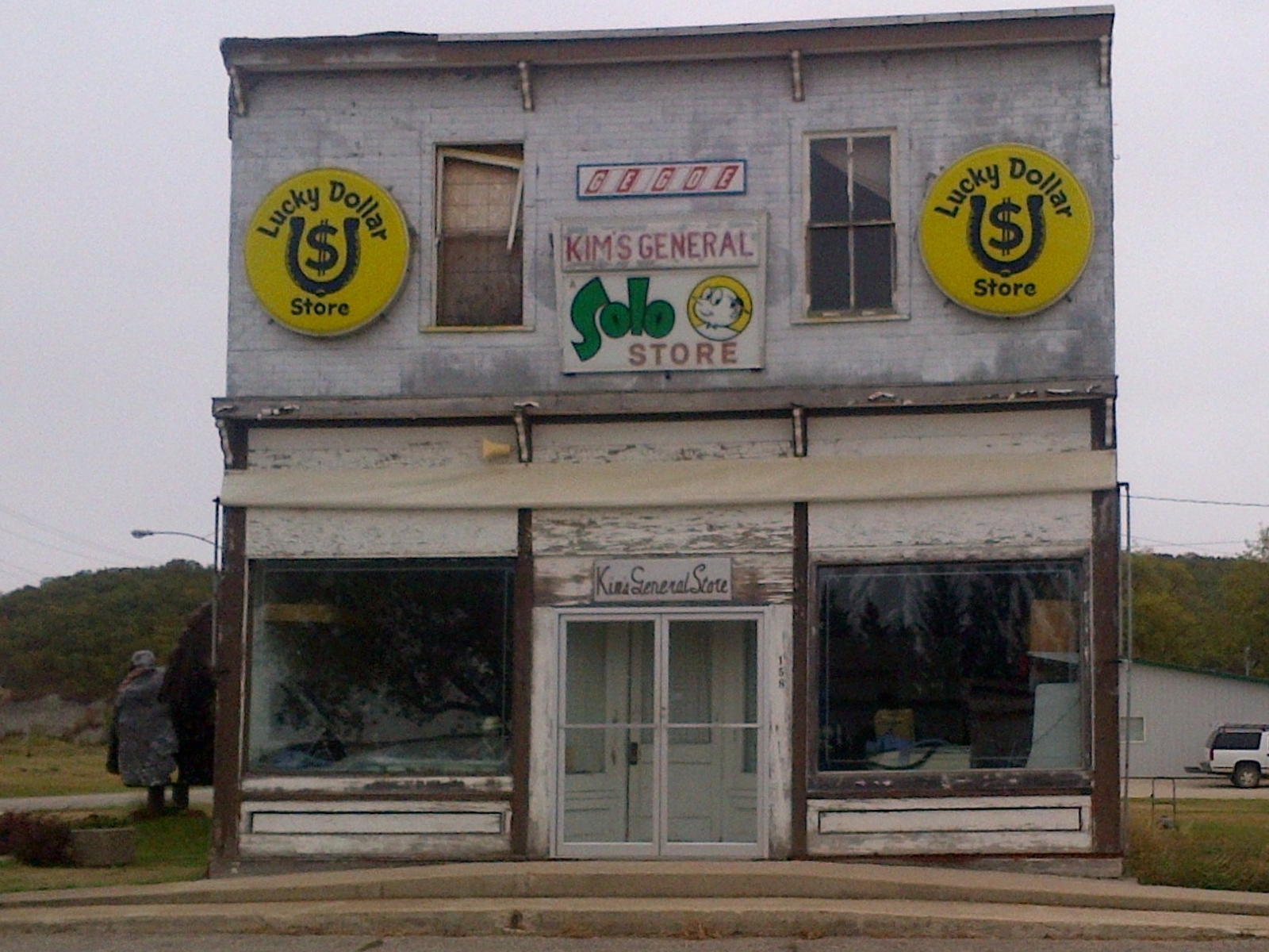 A now abandoned multi storey building with old signage identifying it as "Kim's General / Solo Store / Lucky Dollar Store". To the left of the building is a large turkey statue.