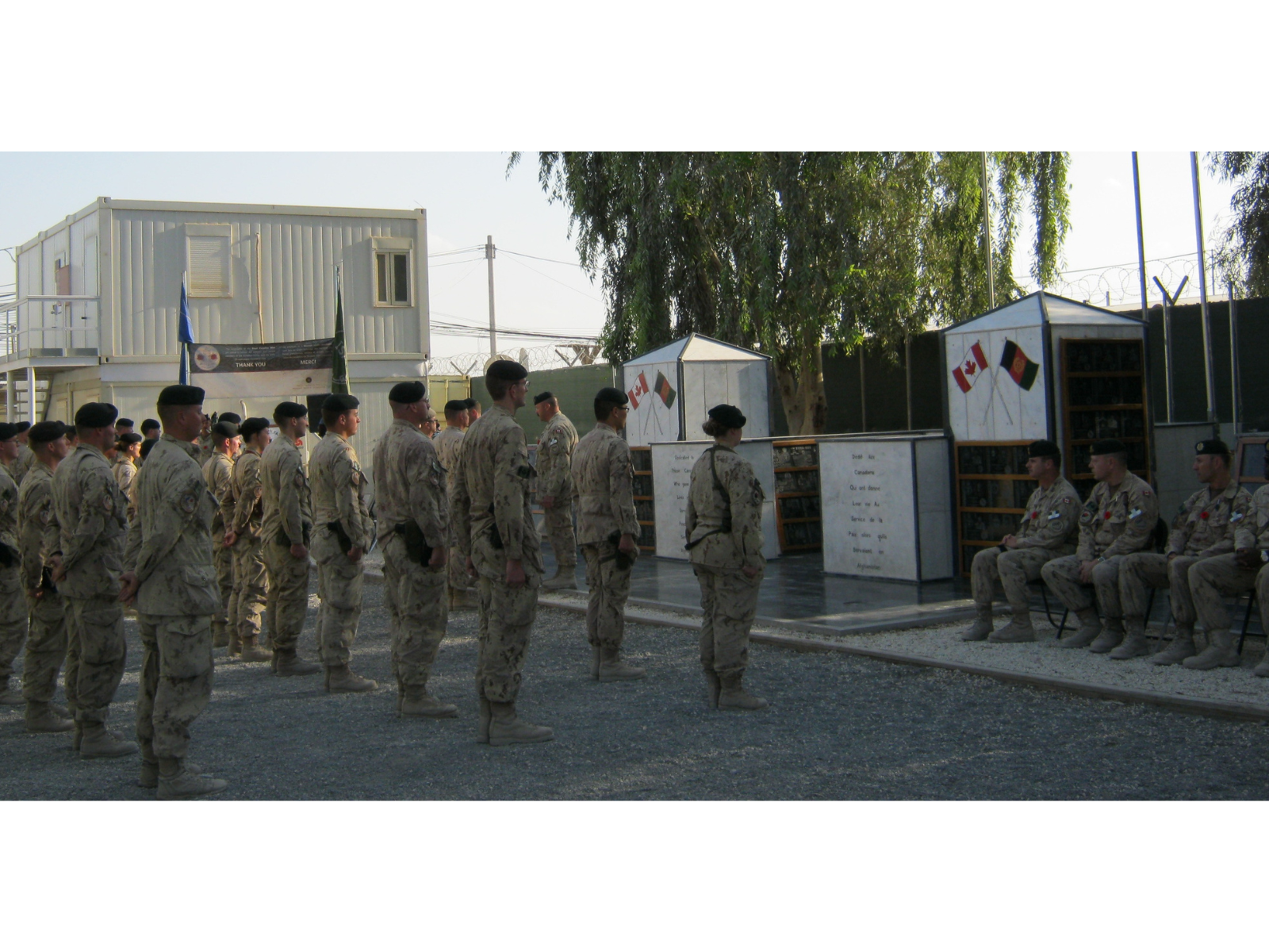 Soldiers in khaki uniforms standing at attention in front of a memorial.
