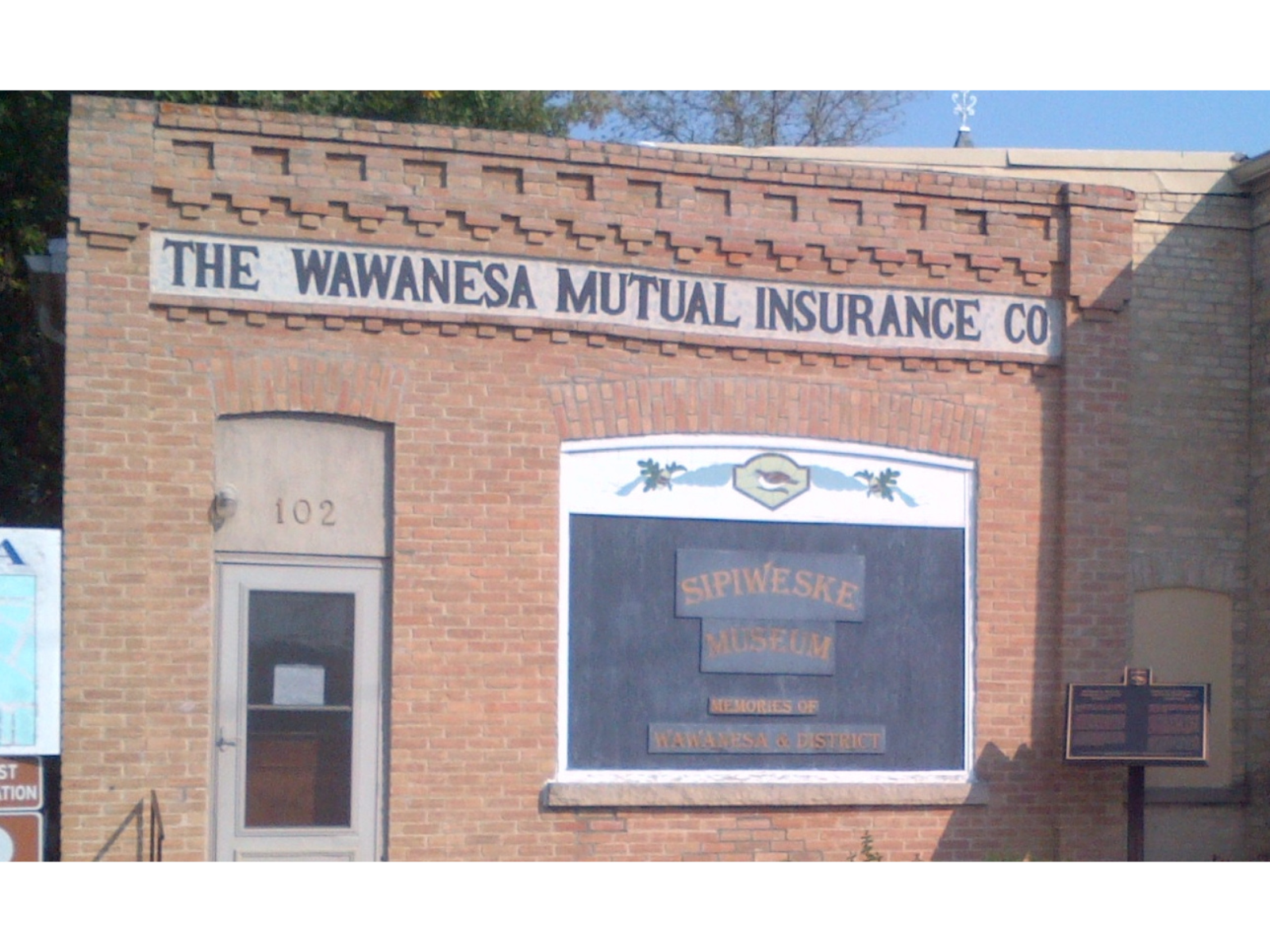 Exterior of a red brick building with a sign across the top reading, "The Wawanesa Mutual Insurance Co". Below it, to the right of the entrance is another sign reading, "Sipiweske Museum".