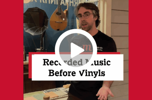 A screenshot of a video, an individual stands in front of an exhibit in the Winnipeg Gallery. There's a play button over the screenshot and overlaid text reads, "Recorded Music Before Vinyls".