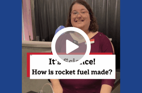 A screenshot of a video, an individual stands in the Science Gallery. There's a play button over the screenshot and overlaid text reads, "It's Science! How is rocket fuel made?".