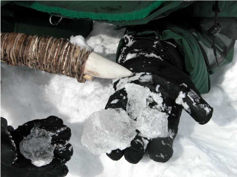 Close up on two mitted hands holding chunks of ice, and the tip of a white antler tool.