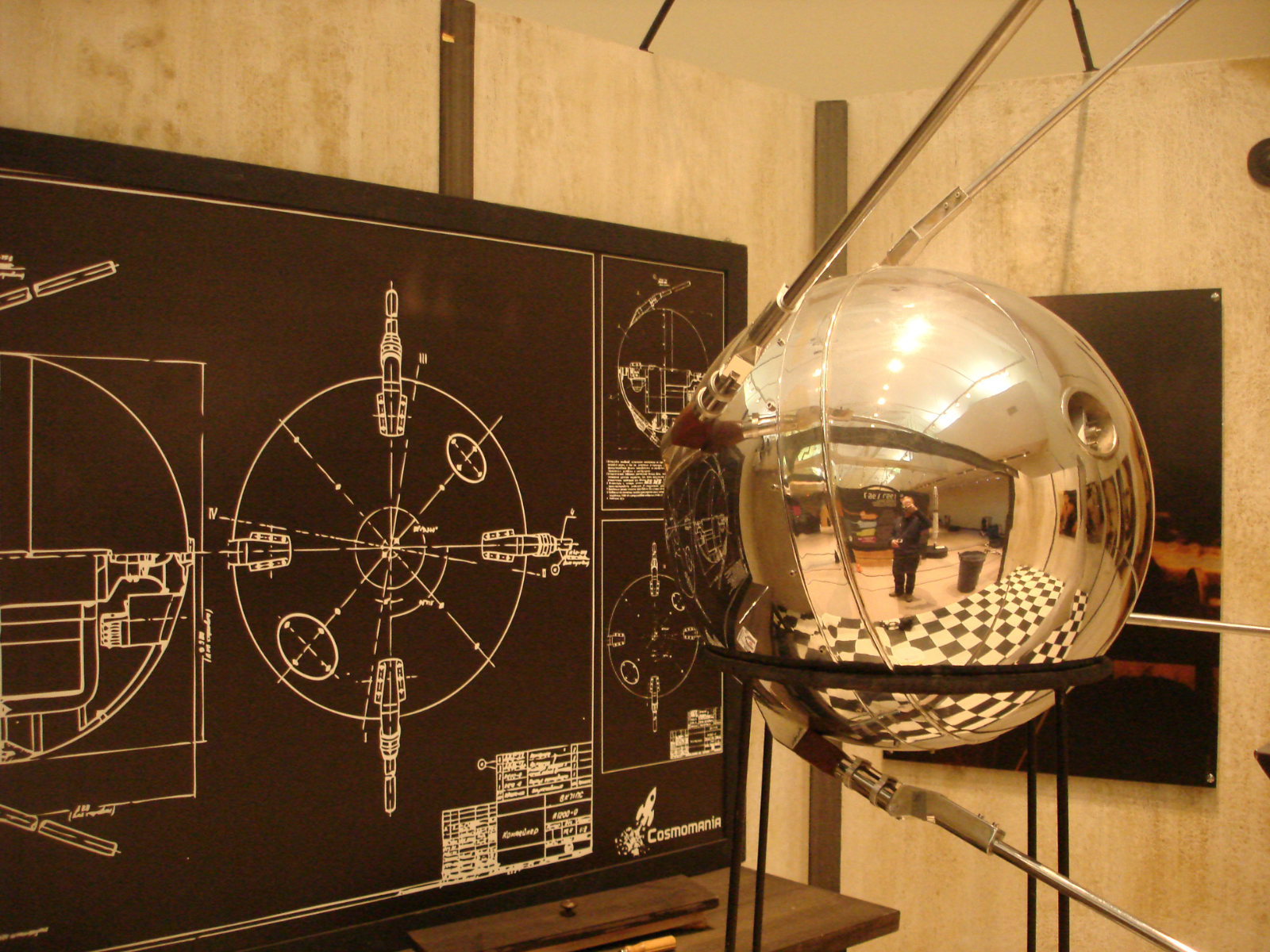 A reflective metal orb on a stand in front of a chalkboard like sign with blueprints on it.