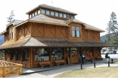 A multi storey wooden building. The main floor consists of primarily windows under an awning stretching the perimeter of the building. Wooden benches are placed periodically under the windows.