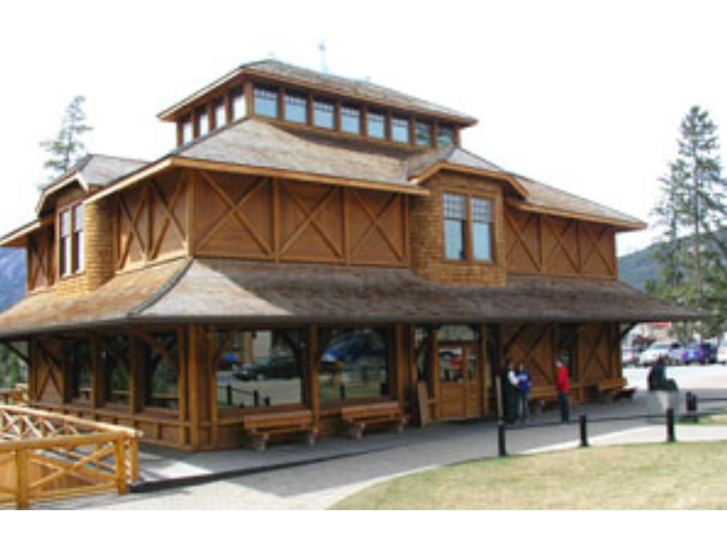 A multi storey wooden building. The main floor consists of primarily windows under an awning stretching the perimeter of the building. Wooden benches are placed periodically under the windows.