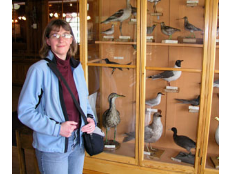 A smiling individual posing beside a display case containing a variety of taxidermized birds.